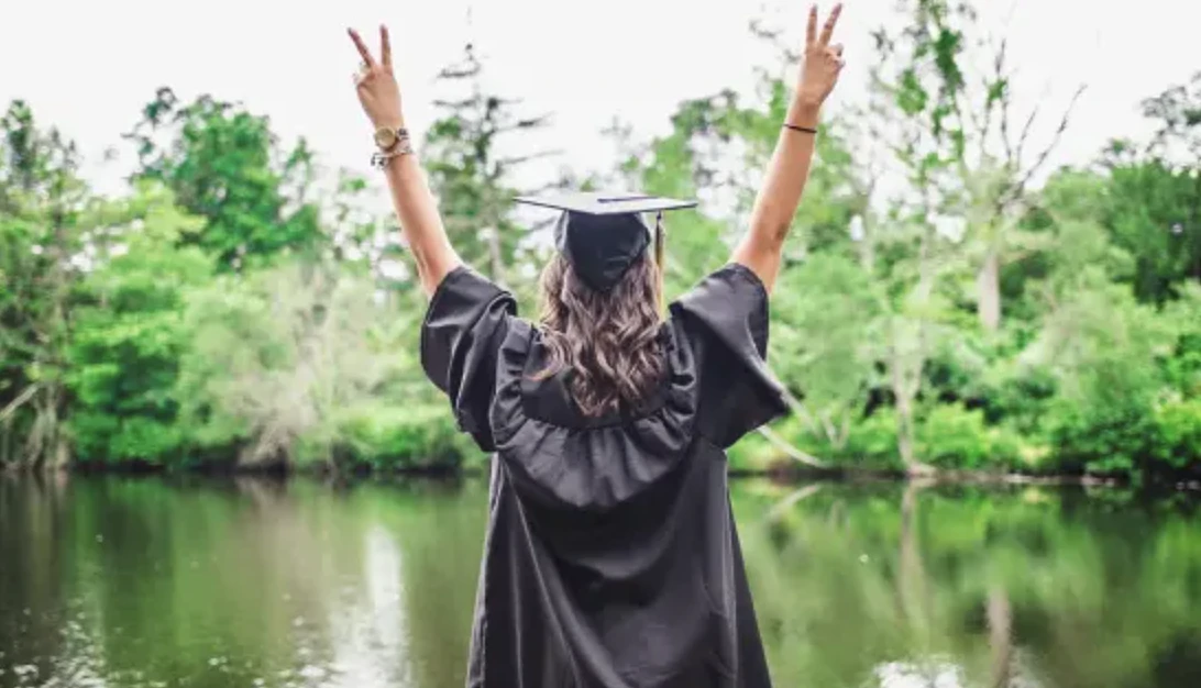 student in graduation robe, facing away from camera holding up peace signs