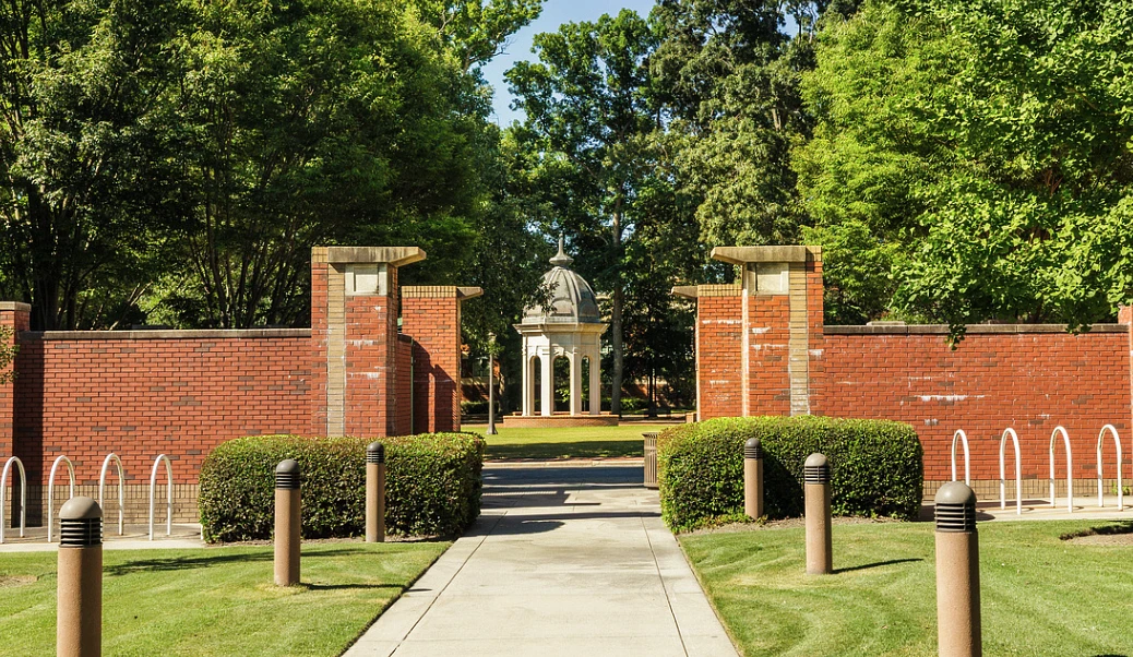 A paved pathway leads through brick walls and greenery to a domed structure in the distance.