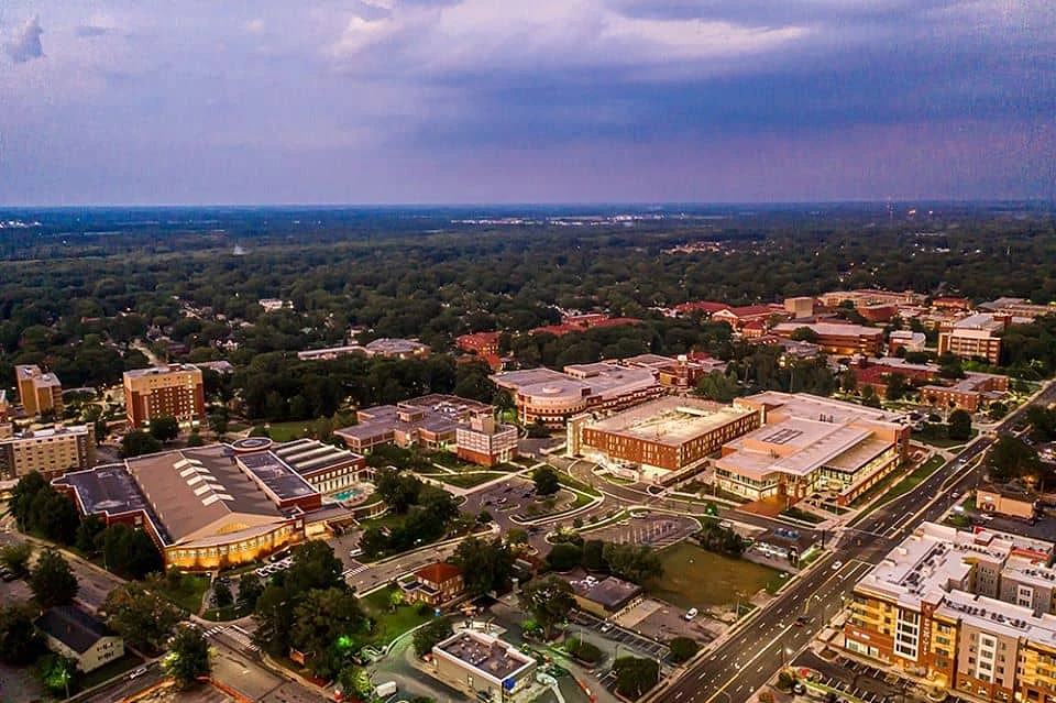 An aerial view of East Carolina. Showcasing its multiple buildings surrounded by lush greenery under a purple sunset.