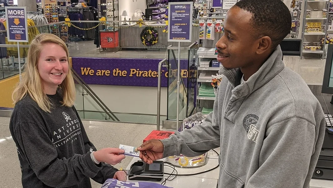 A man and woman are smiling at a checkout counter in a university store.