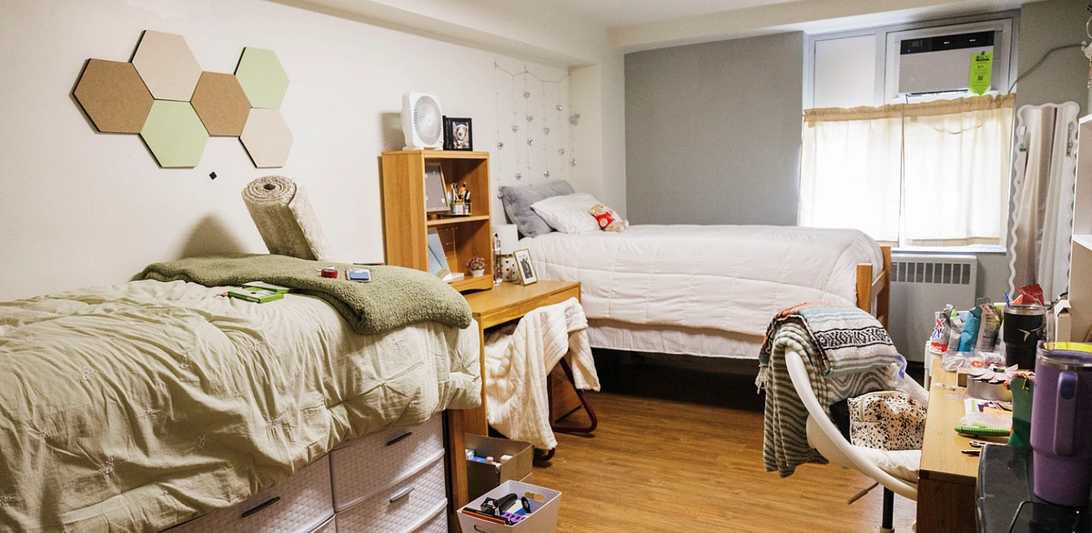 A neatly organized dorm room with two beds, a wooden desk, and various personal items scattered around.